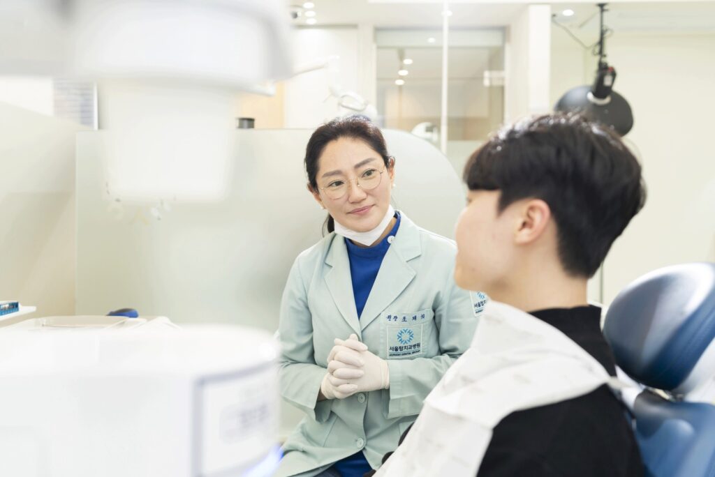 서울탑치과병원 교정 원장이 진료 의자에 앉은 환자와 마주 보며 상담하는 모습 (환자 뒷모습)